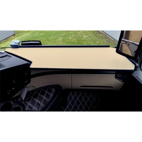 Armaturenbrettansicht eines Fahrzeuginnenraums von Mercedes mit beigem LKW-Tisch mit schwarzem Rand. Das Lenkrad und der Sitz mit Rautenmusterbezug sind sichtbar. Das Fenster zeigt eine Rasenfläche draußen.