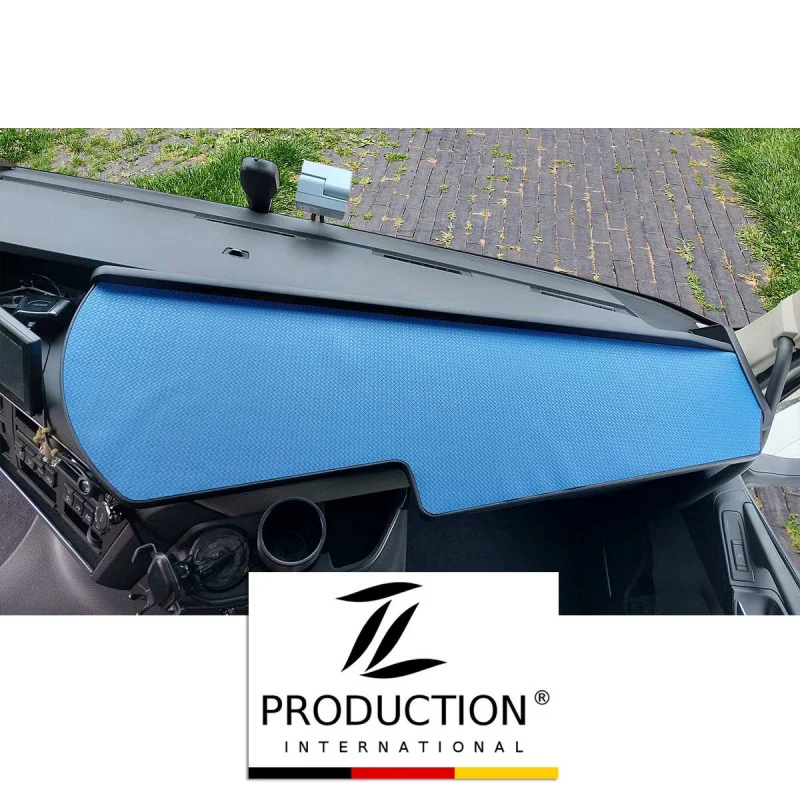 Das LKW-Tisch für den Volvo FH ist elegant mit einer blauen Antirutschmatte bedeckt. Der Blick umfasst Teile der Windschutzscheibe und des Seitenspiegels. Ein Logo am unteren Rand zeigt „TL Production International“, während die Matte einen starken Kontrast zum dunklen Innenraum bildet.