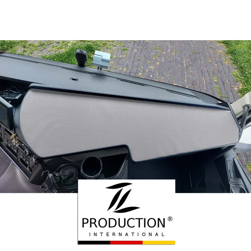 Das Armaturenbrett des Fahrzeugs, ausgestattet mit einem LKW-Ablagetisch und einer eleganten grauen Schutzabdeckung, bietet durch die Windschutzscheibe einen Blick auf den gepflasterten Außenbereich. Unten ziert ein Logo mit der Aufschrift „Production International“ das Volvo FH-Erlebnis mit einem Hauch von Eleganz.