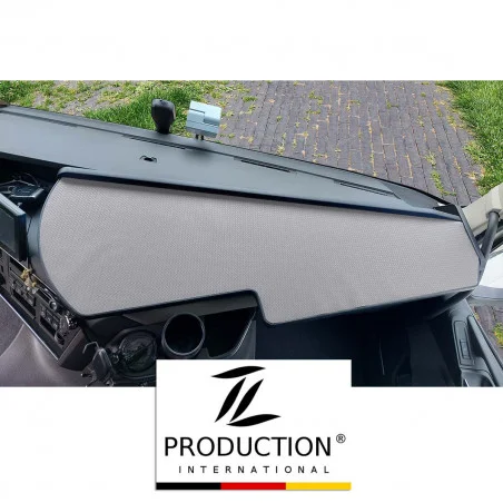 Das Armaturenbrett des Fahrzeugs, ausgestattet mit einem LKW-Ablagetisch und einer eleganten grauen Schutzabdeckung, bietet durch die Windschutzscheibe einen Blick auf den gepflasterten Außenbereich. Unten ziert ein Logo mit der Aufschrift „Production International“ das Volvo FH-Erlebnis mit einem Hauch von Eleganz.